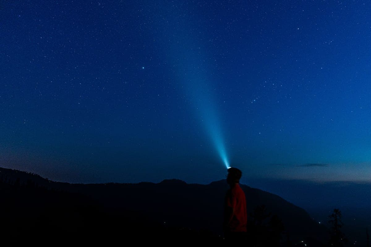 A runner on a trail at night lit by a headlamp beam